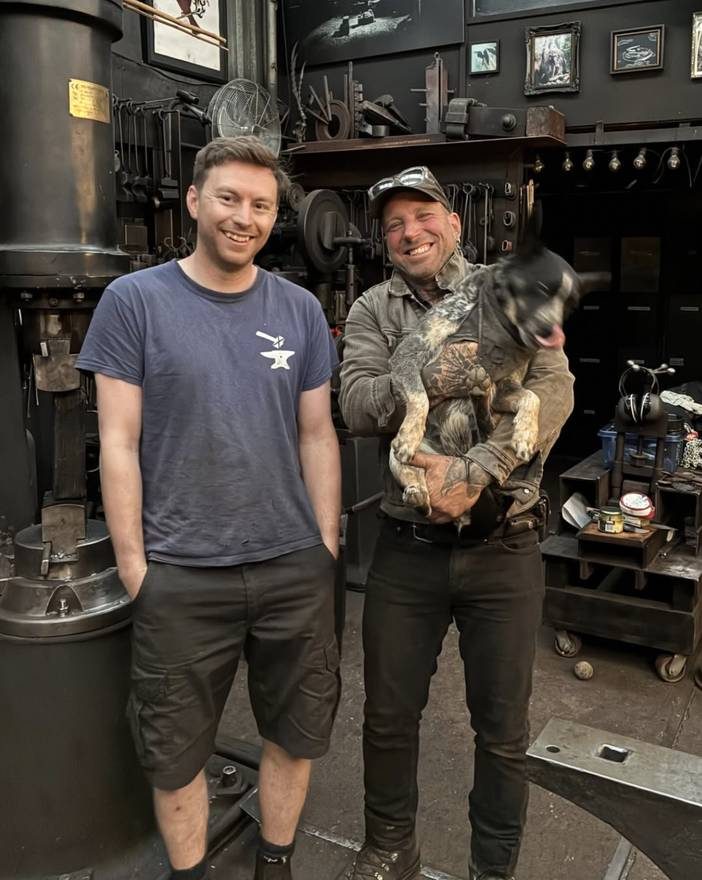 Sandy in the forge with a fellow blacksmith and a dog
