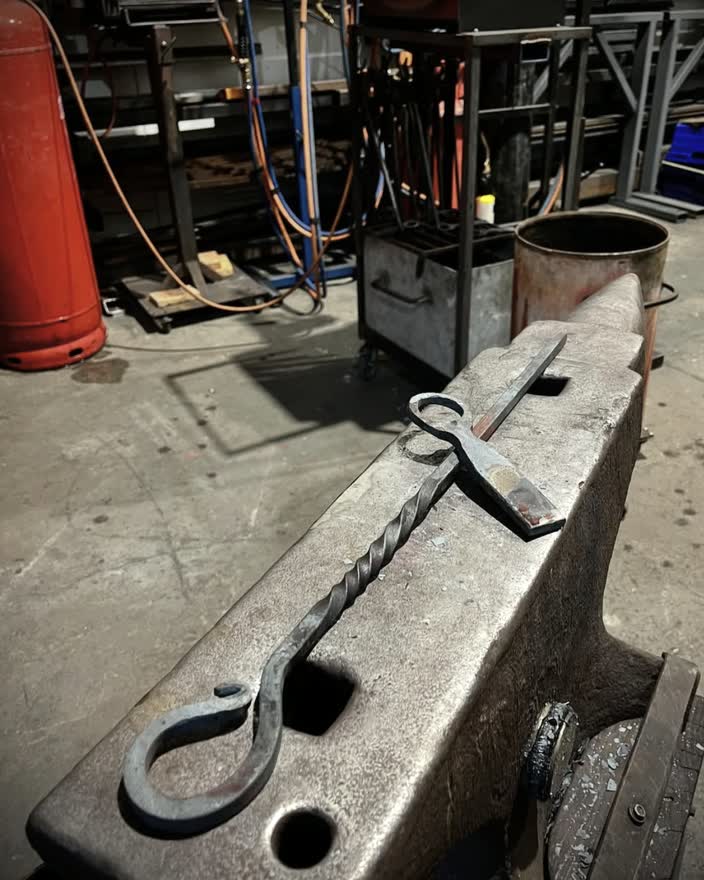 A hand forged hook with a twisted shank resting on the anvil