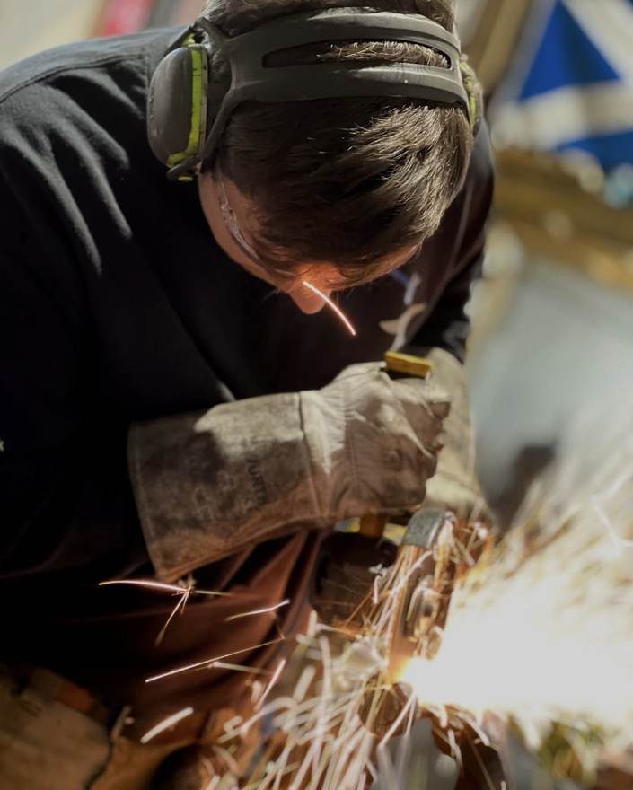 Grinding a forged piece, sparks flying, saltire on the workshop wall